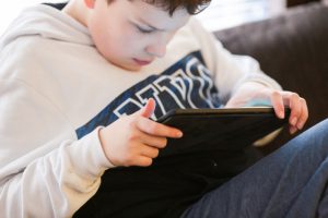 Poika istuu sohvalla ja selaa tablettia. Lyhytaikaishoito Haminan Ravimäessä mahdollistaa mukavan paikan omaishoidettavalle omaishoitajan vapaan ajaksi.