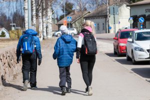 Kaksi lasta kävelee ohjaajan saattamana kevätvaatteissa iltapäivähoitoon Ravimäkeen. Iltapäiväkerho Haminan Ravimäessä toimii kouluvuoden aikana maanantaista perjantaihin.