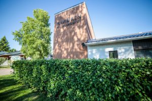 Ravimäkiyhdistyksen piha, sisääntulo, kyltti ja vehreä pensasaita. Ravimäkiyhdistys palvelee Haminassa Tarkka-ampujankadulla. Liity jäseneksi tai hae töihin!