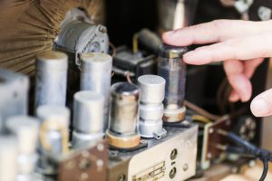 Hyvin vanha elektroninen laite johtoineen. Miehen käsi koskettaa laitteen osaa. Haminassa pienkonehuolto onnistuu myös Ravimäen Työpalvelussa.